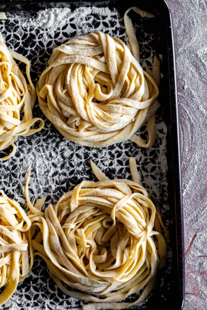 Sourdough pasta noodles rolled into nests on a floured baking sheet.