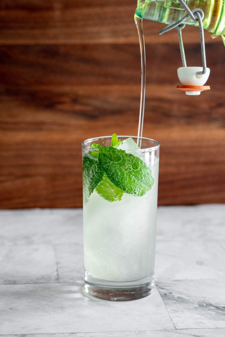 Pouring smoked simple syrup into a mojito.