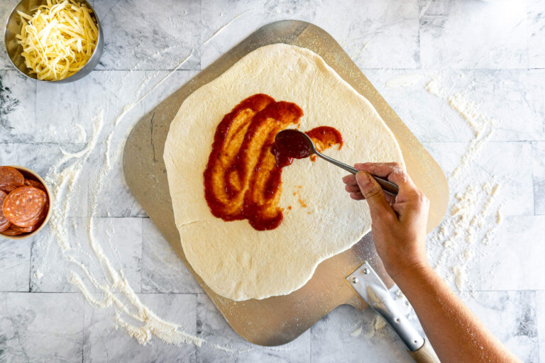 Smearing the pizza dough with pizza sauce.