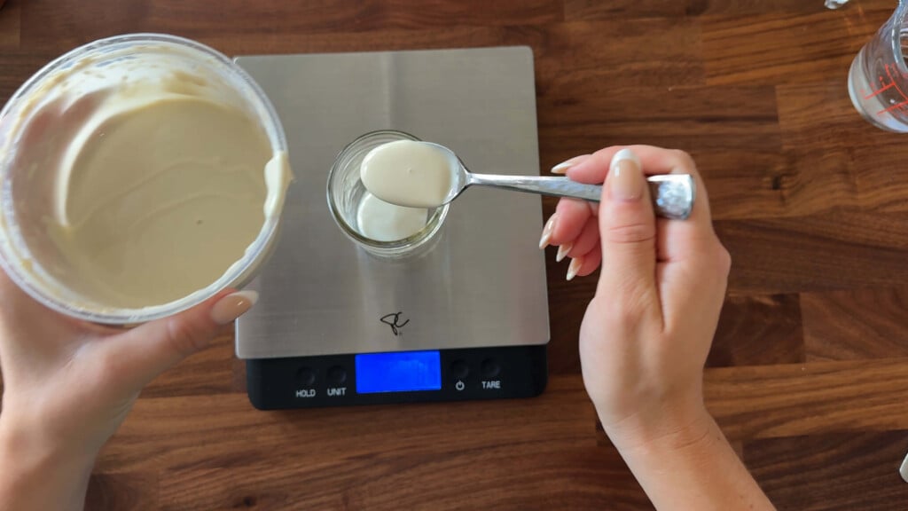 Measuring sourdough starter and adding to a clean jar.
