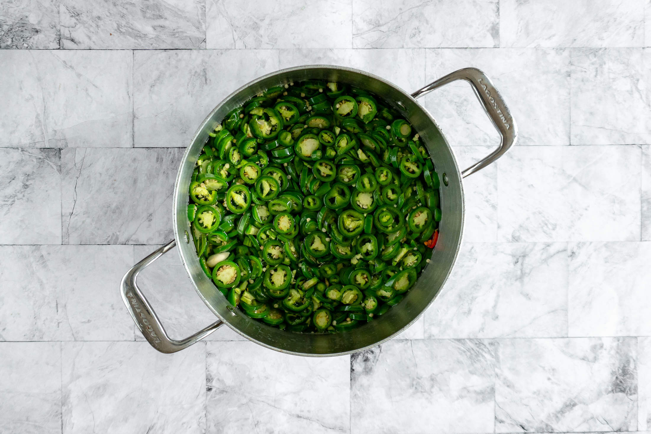 Sliced jalapeño rings and garlic added to boiling pickling brine. 