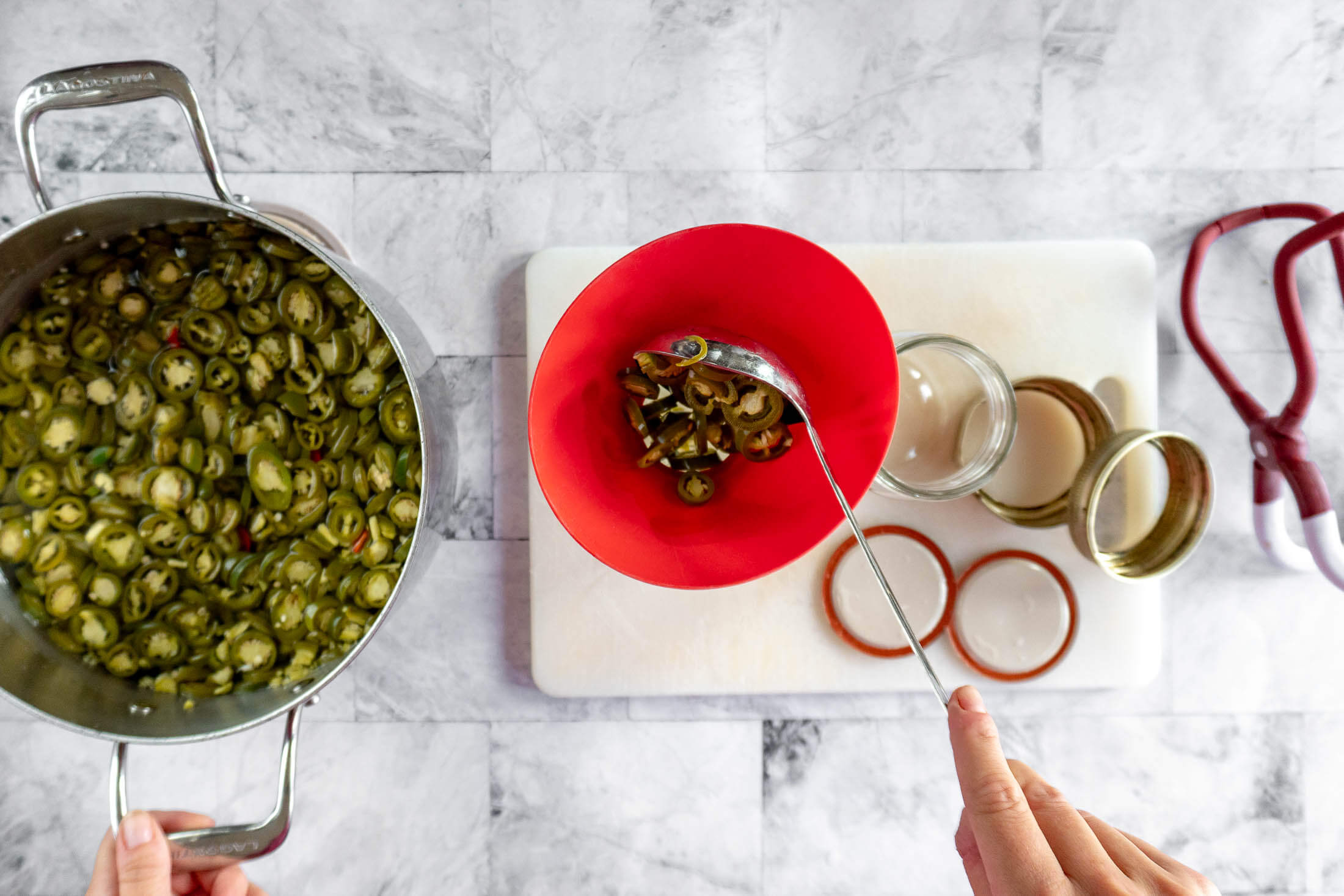 Ladling hot brined jalapenos into a pint jar through a canning funnel. 