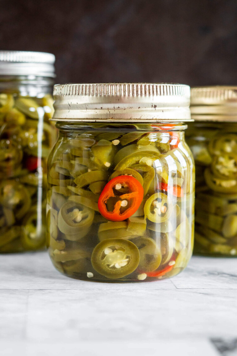 A jar of pickled jalapenos with a ring from one red jalapeno.