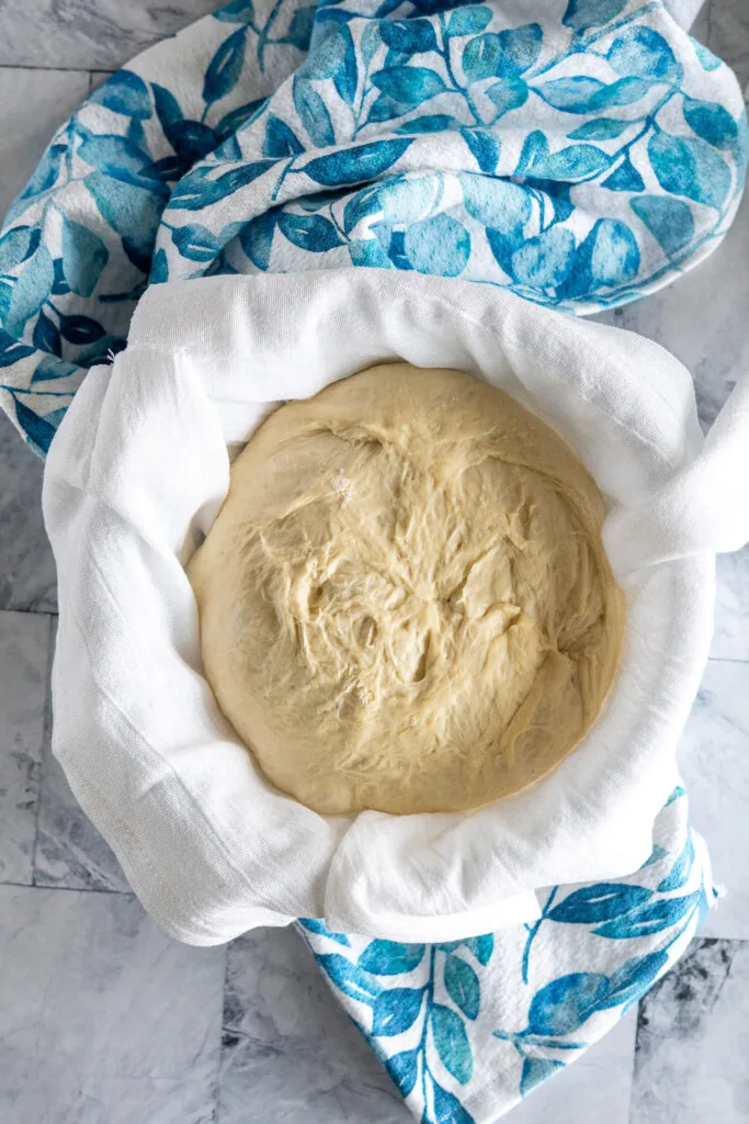 Proofing dough in glass bowl lined with flour sack towel.