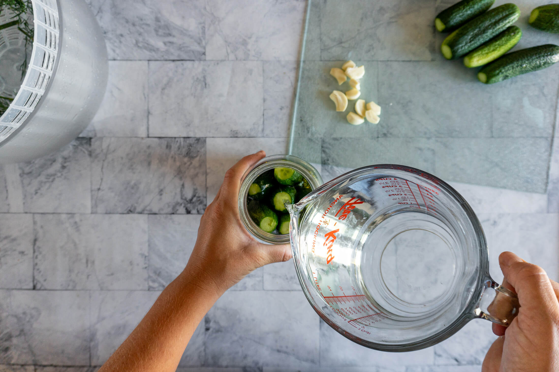 Pouring salt brine cucumbers, dill, and garlic in a jar. 