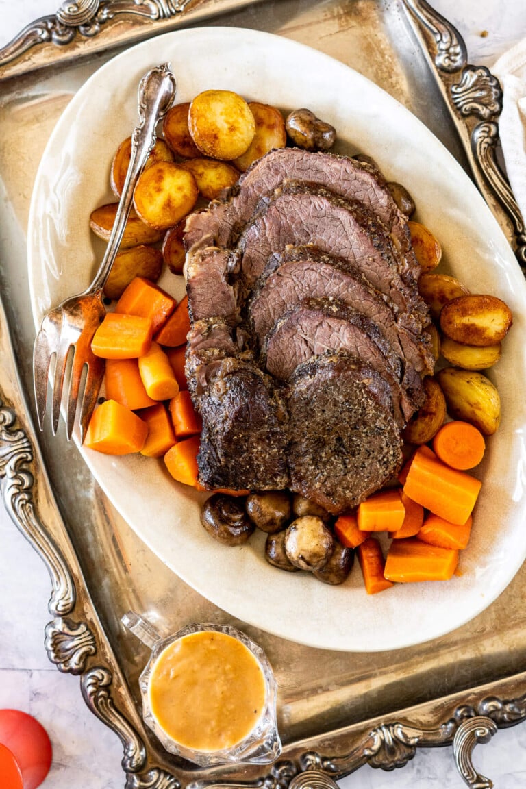 Sliced cross rib roast on a serving platter with potatoes, carrots and mushrooms.