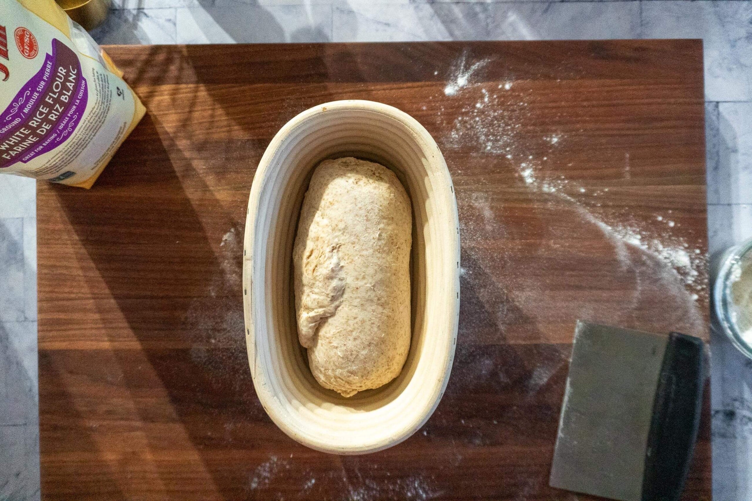 Shaped whole wheat sourdough loaf resting seam-side up in a banneton.