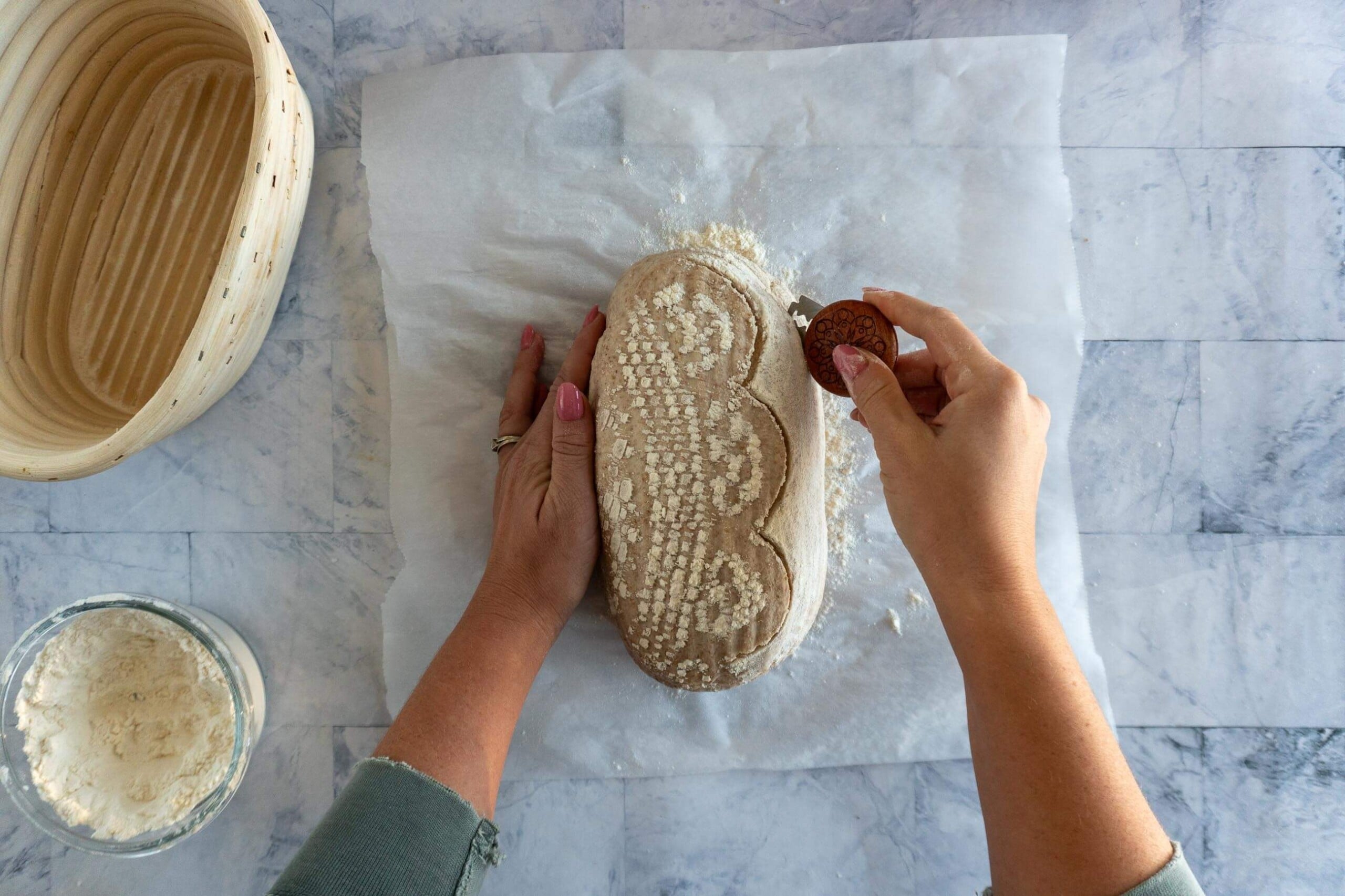 Scoring a whole wheat sourdough loaf with a curved slash before baking.