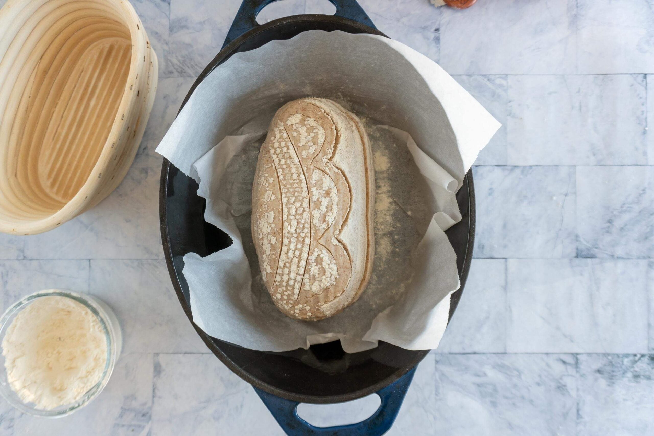 Whole wheat sourdough loaf on parchment paper being transferred into a preheated dutch oven.