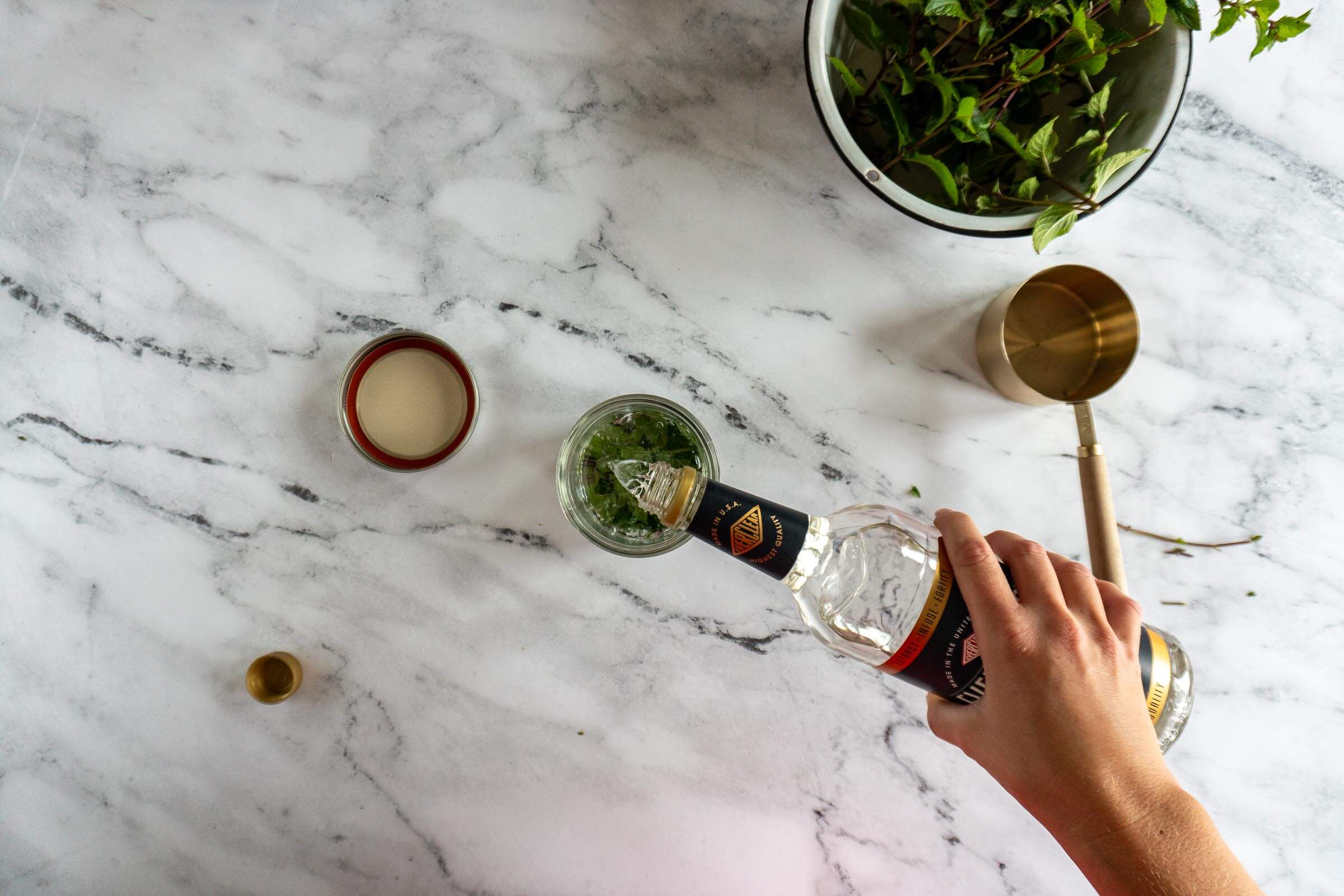 Pouring high proof alcohol over mint leaves in a small mason jar.