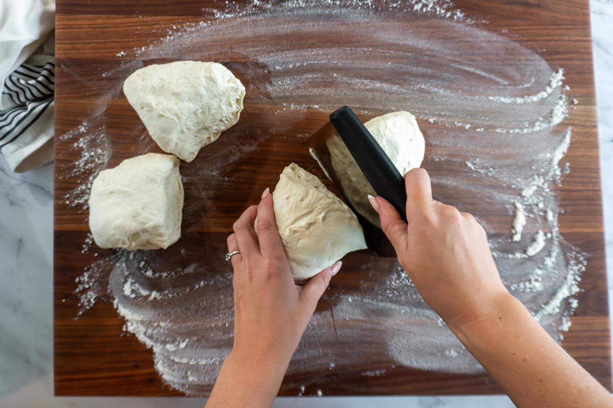 Sectioning sourdough into 4 pieces with a bench scraper.