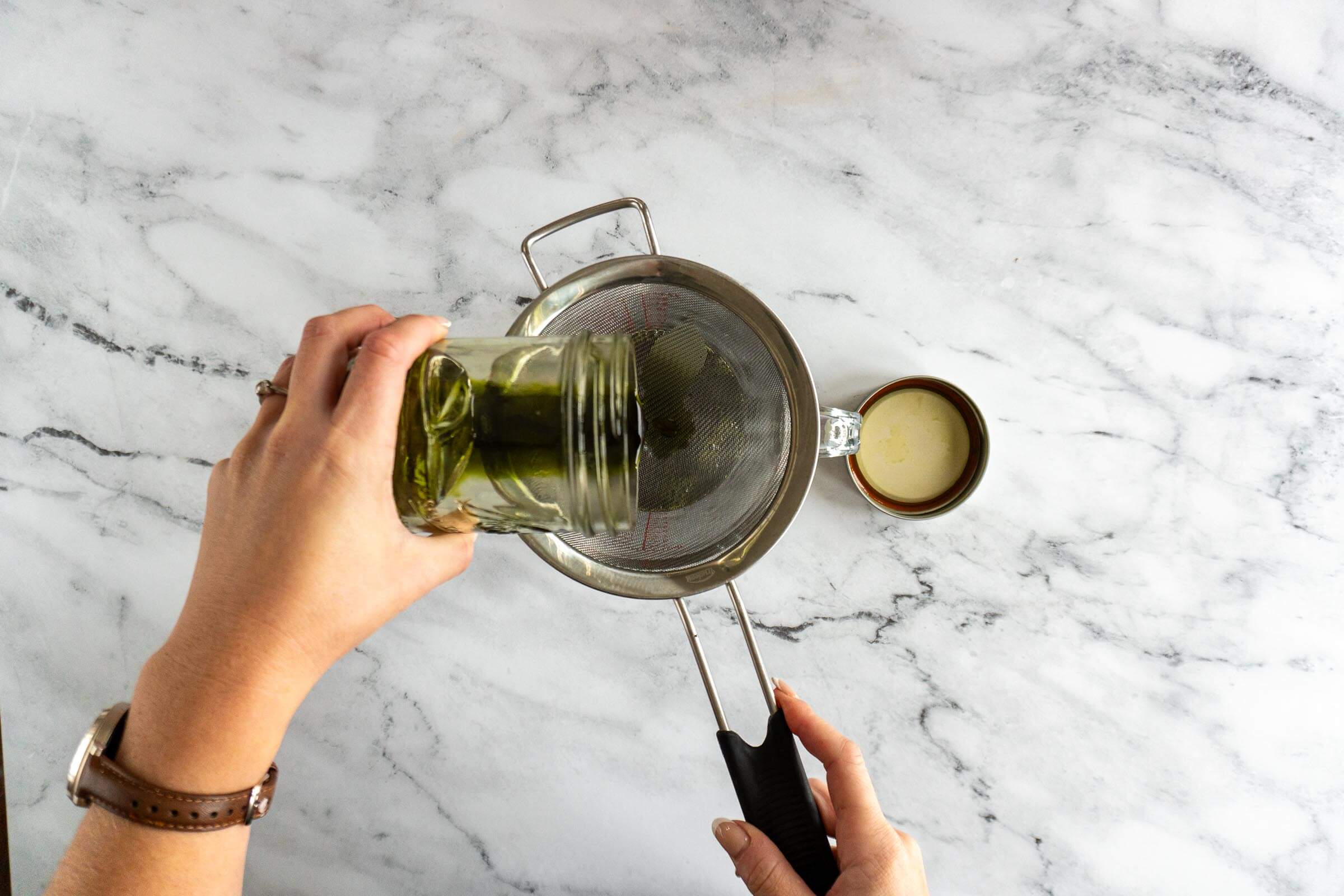 Pouring mint infused alcohol over mesh strainer.