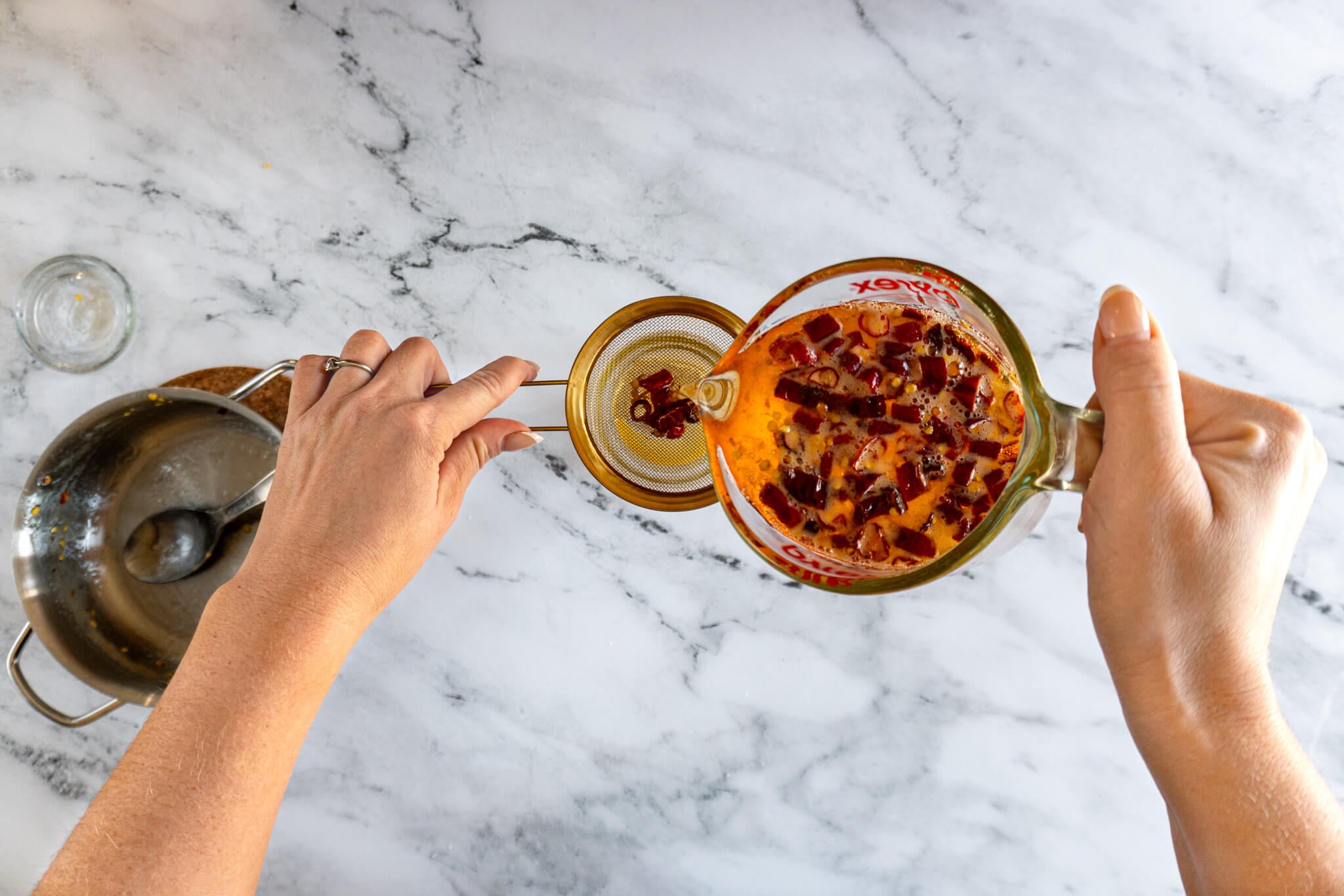 Pouring infused hot honey through a strainer into a storage jar. 