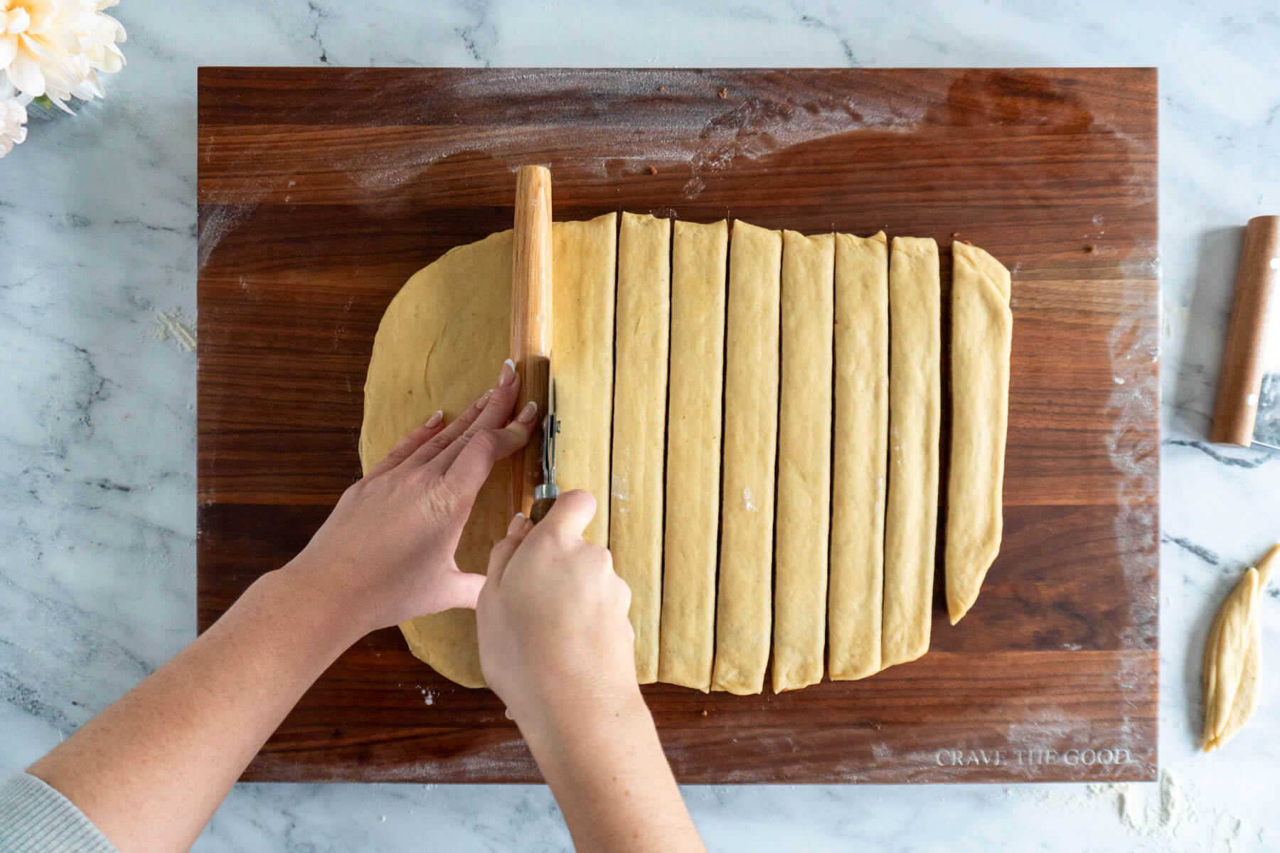 Using a rolling pin as a guide for cutting the dough into strips. 