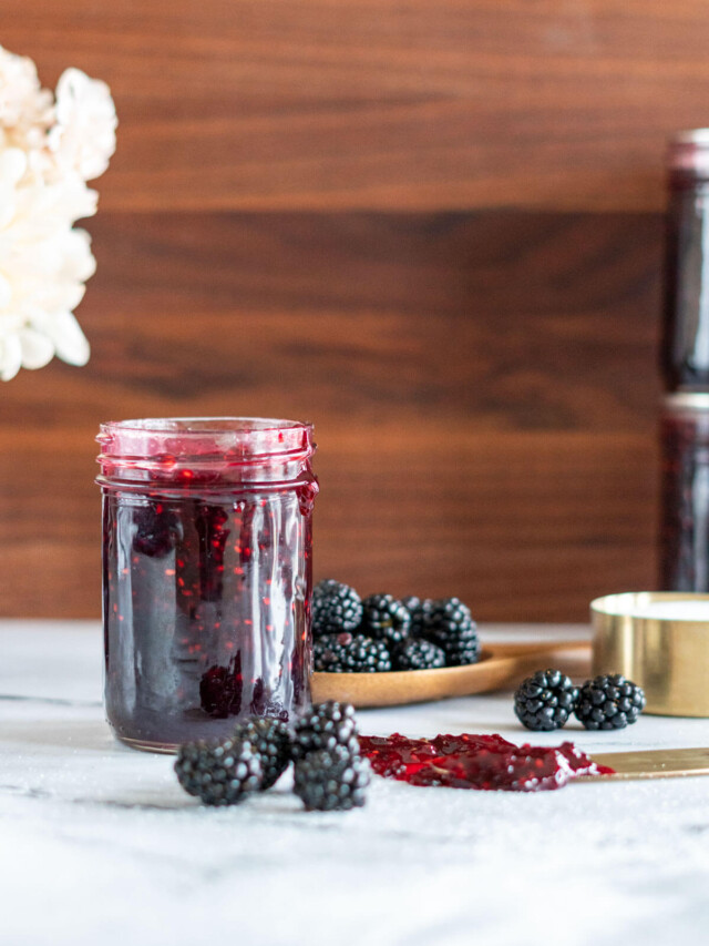 An open jar of blackberry jam with fresh blackberries around it.