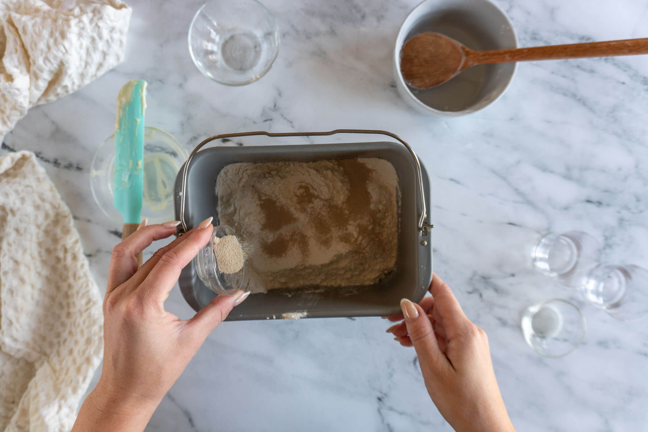 Bread flour and instant yeast being layered on top of the liquids in a bread machine pan. 