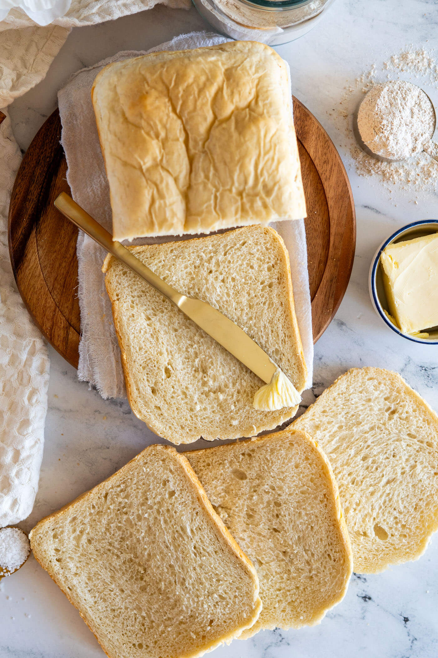 Gold knife spreading butter on a slice of bread machine sourdough. 