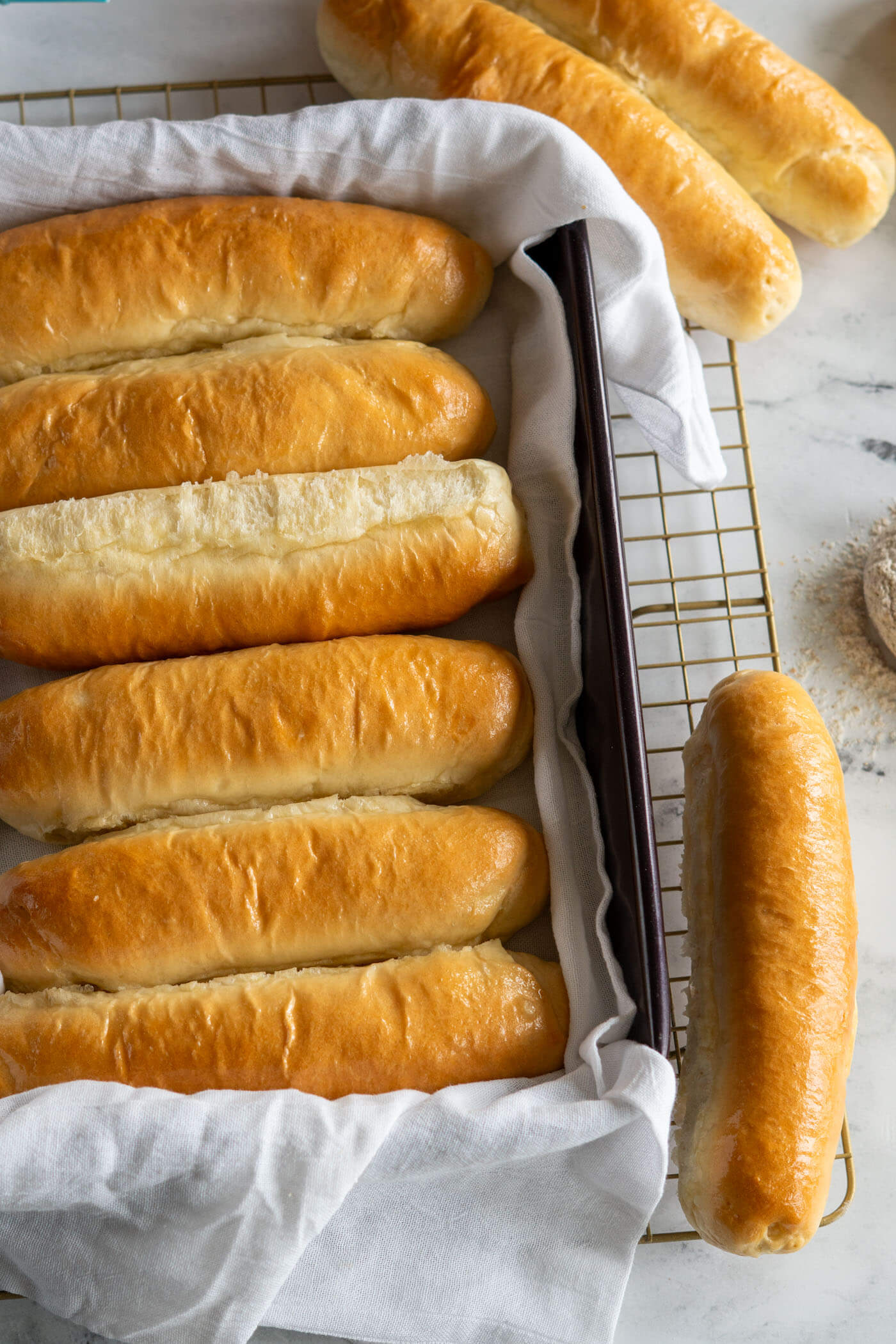 Homemade sourdough hot dog buns on a baking sheet. 