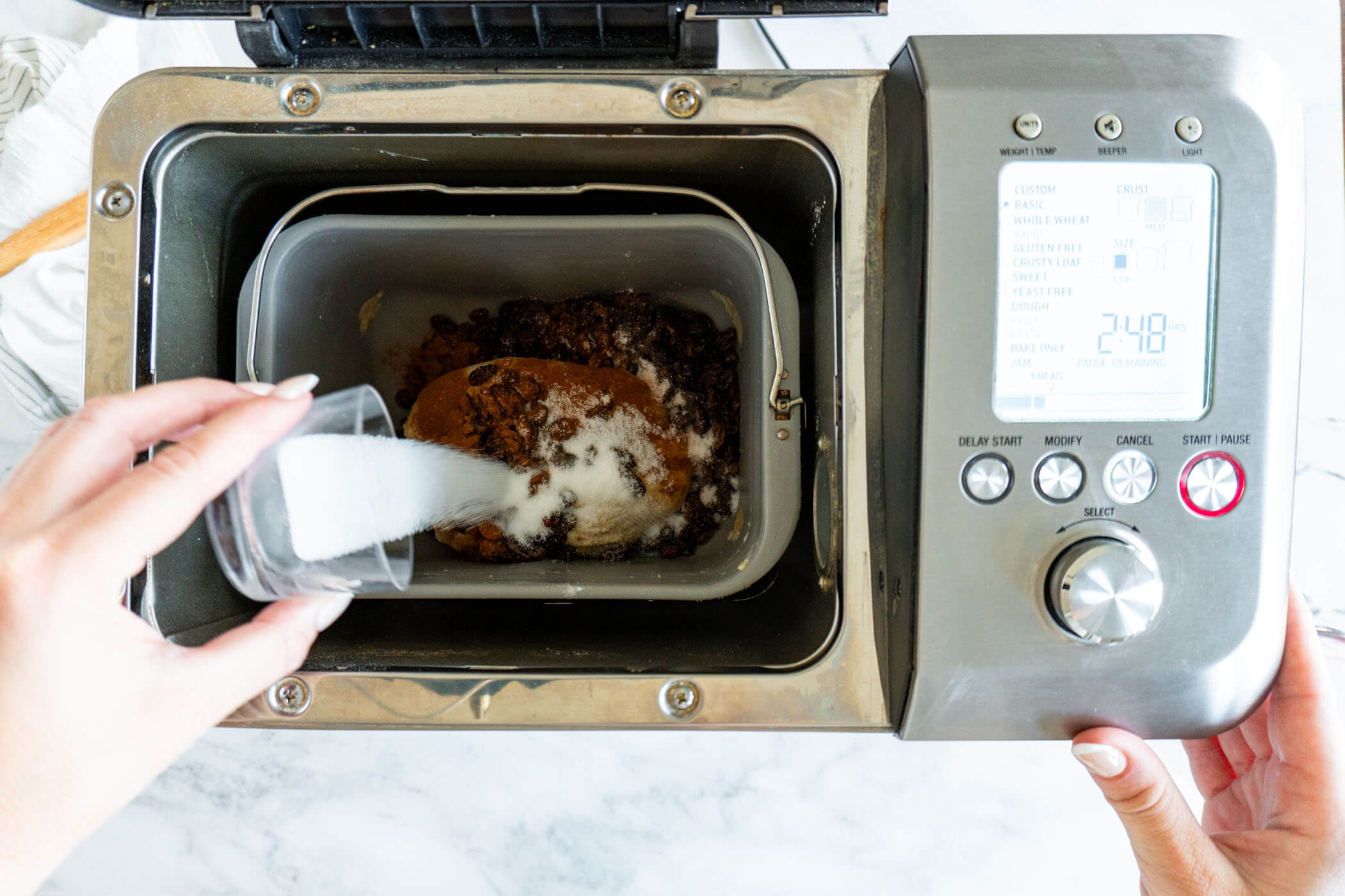 Adding raisins, sugar, and cinnamon to bread pan.