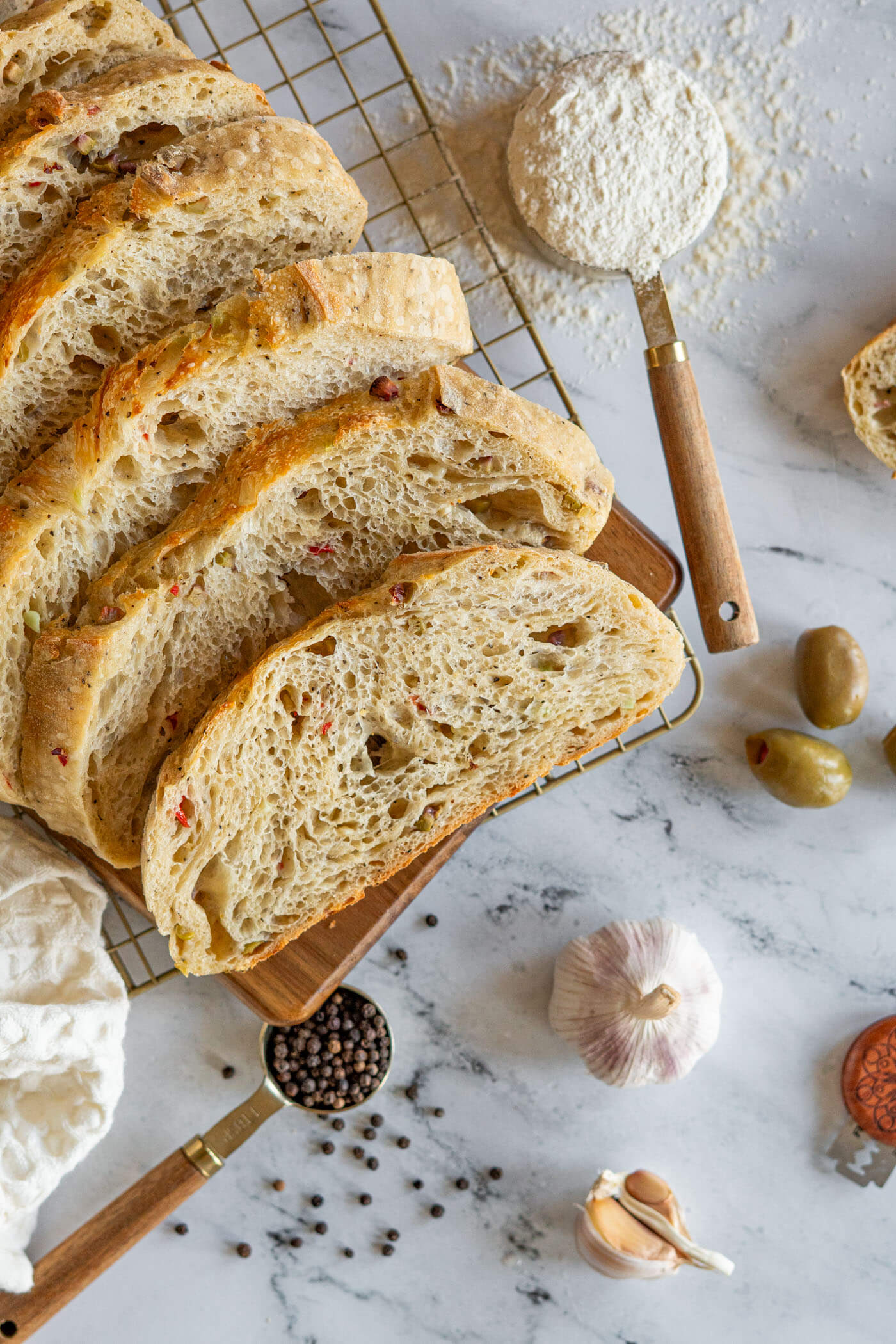 Sliced olive sourdough bread with raw garlic, green olives, and black peppercorns. 