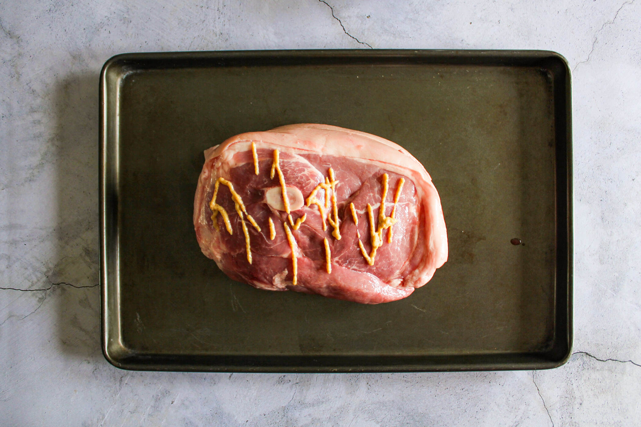 Pork picnic roast on a baking sheet with mustard.