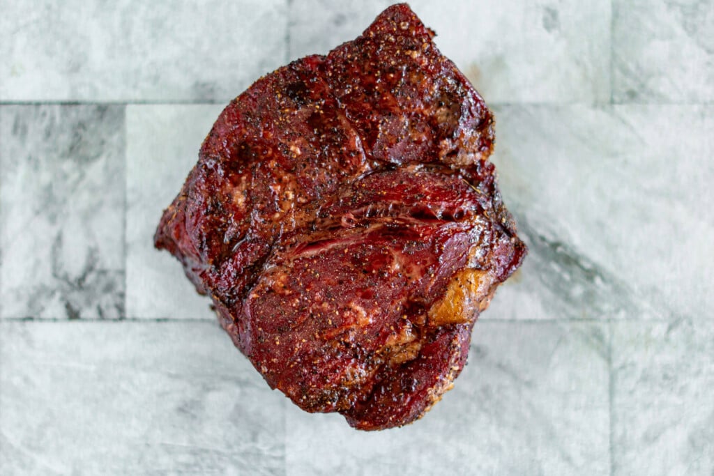 Fully cooked smoked roast beef on a glass cutting board.